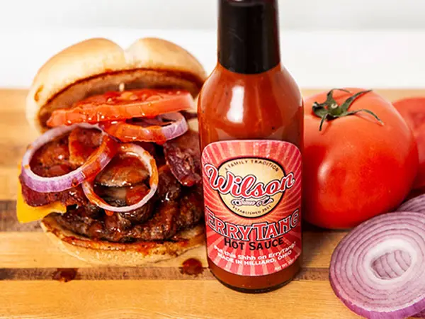 Wilson Burger stacked with melted American cheese and signature EryTang sauce, served next to a bottle of ErryTang Hot Sauce on a wood table