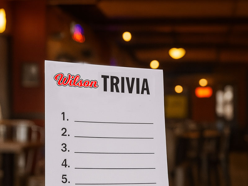Trivia quiz sheet on a wooden table with guests in the background during trivia night at Wilson’s Grill in Hilliard, Ohio